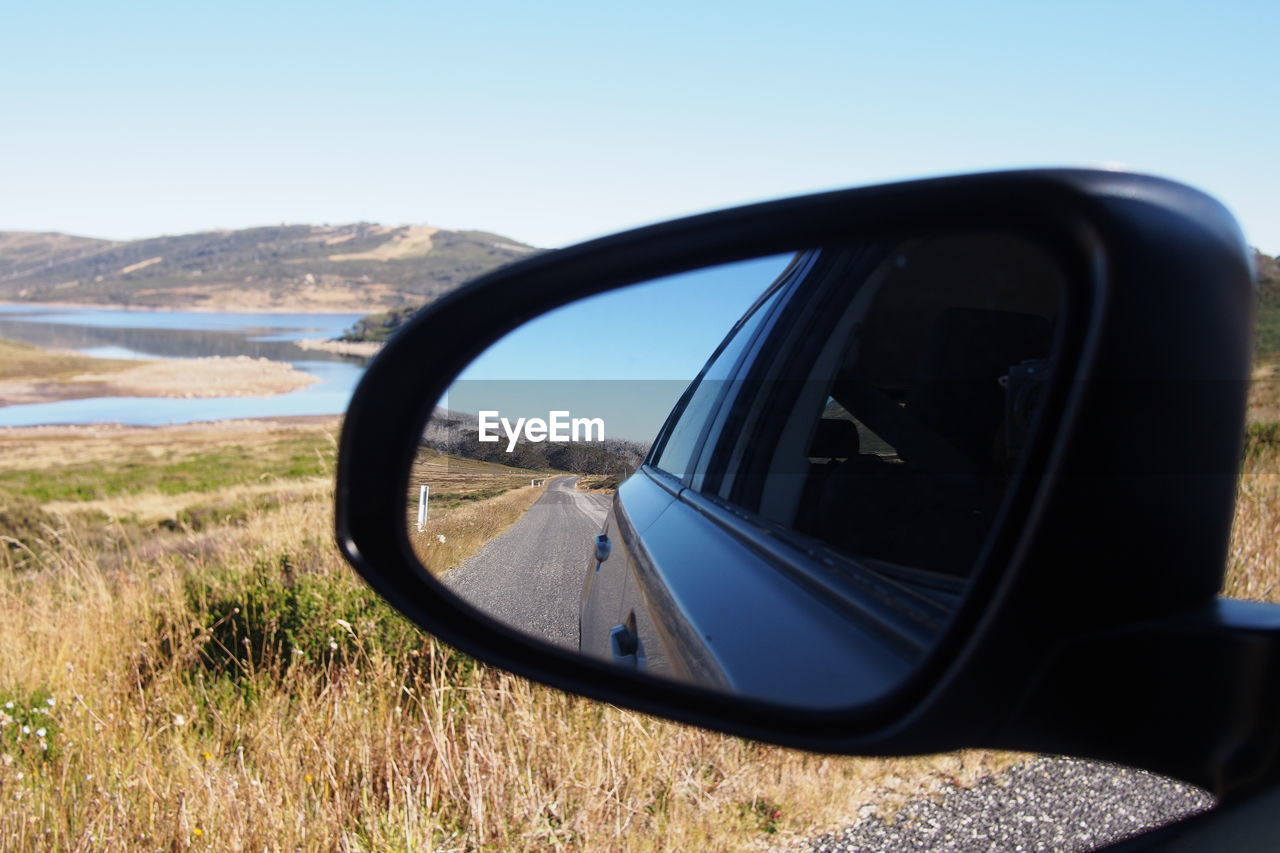 Car reflecting in side-view mirror on road against clear sky