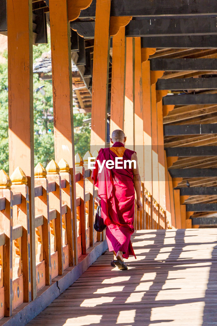 Rear view of monk walking on covered bridge