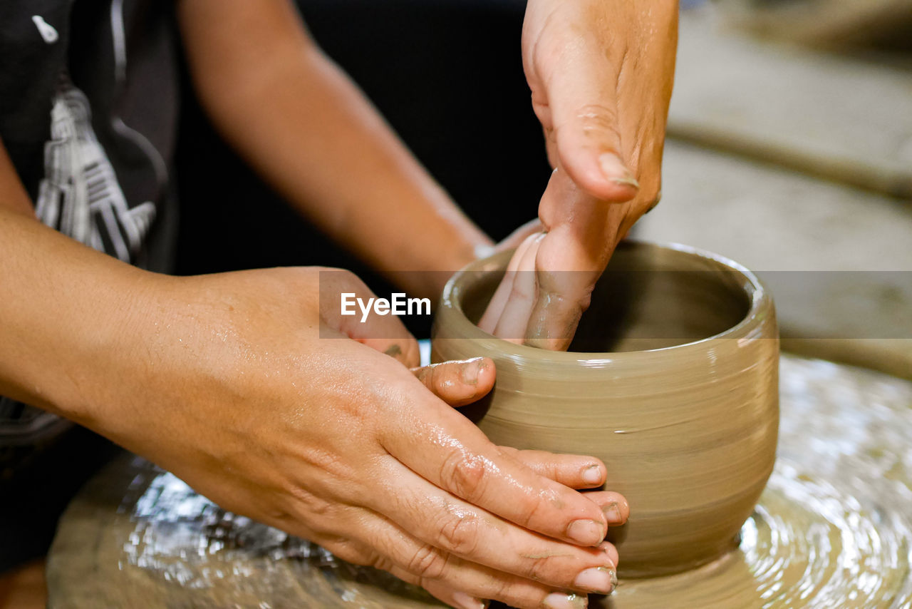 Midsection of people working on pottery wheel