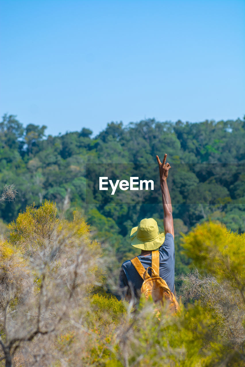 Rear view of a man standing on in the forest against clear sky showing peace sign