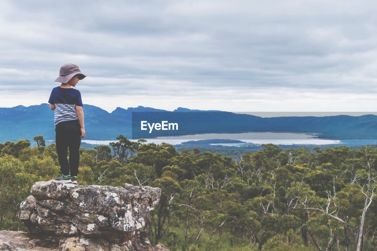 Child standing on rock looking at mountains against sky