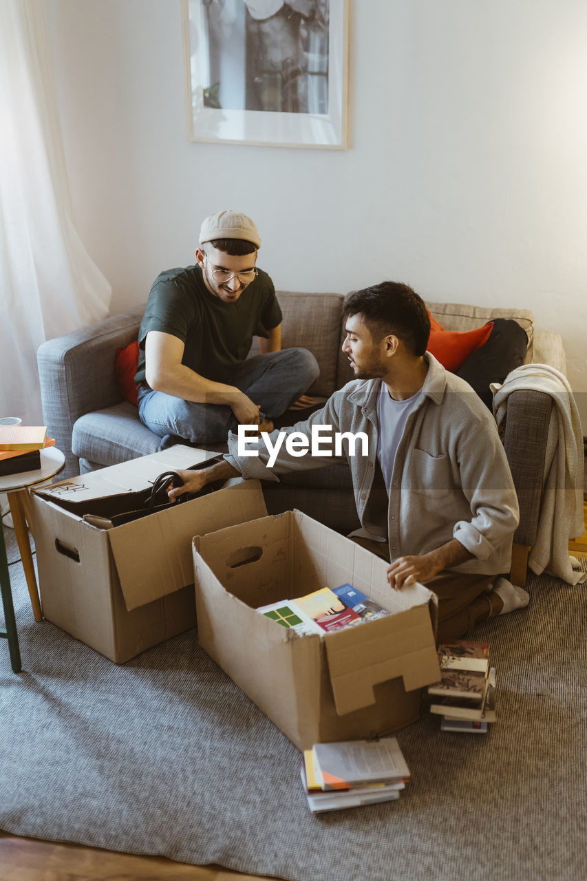 Gay couple talking to each other while unpacking cardboard boxes at home