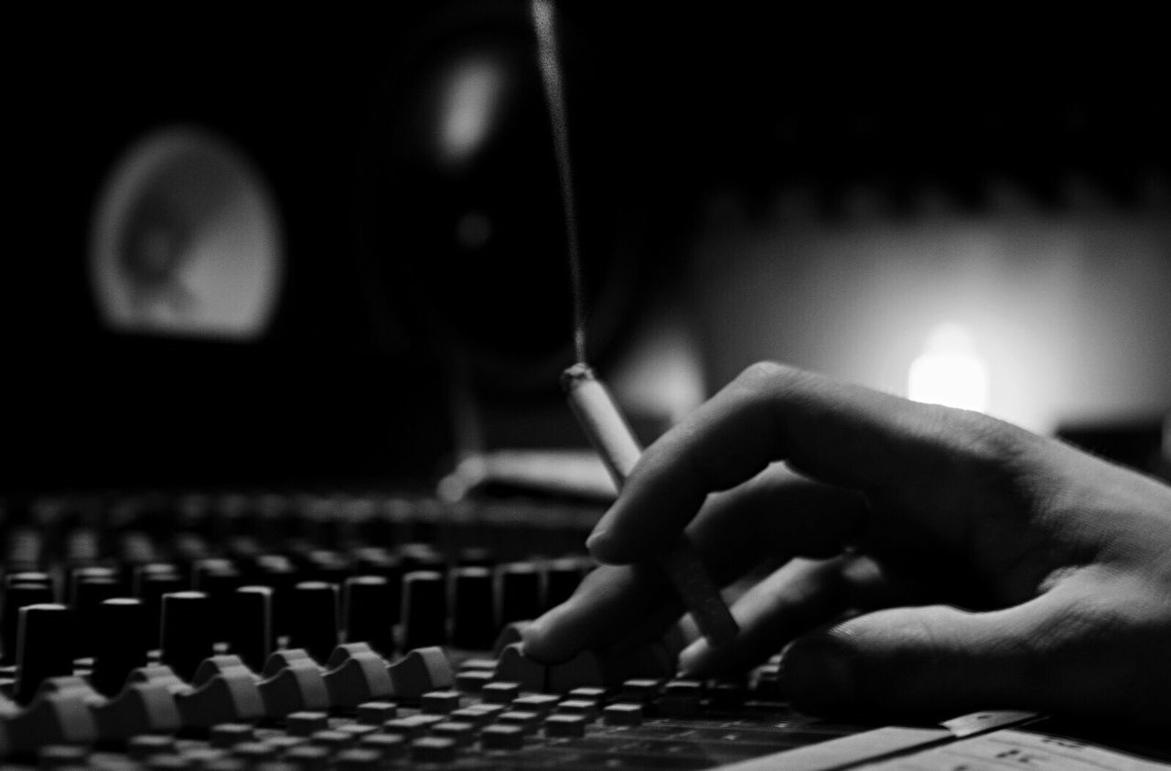 Cropped hand of musician with cigarette using sound mixer at recording studio