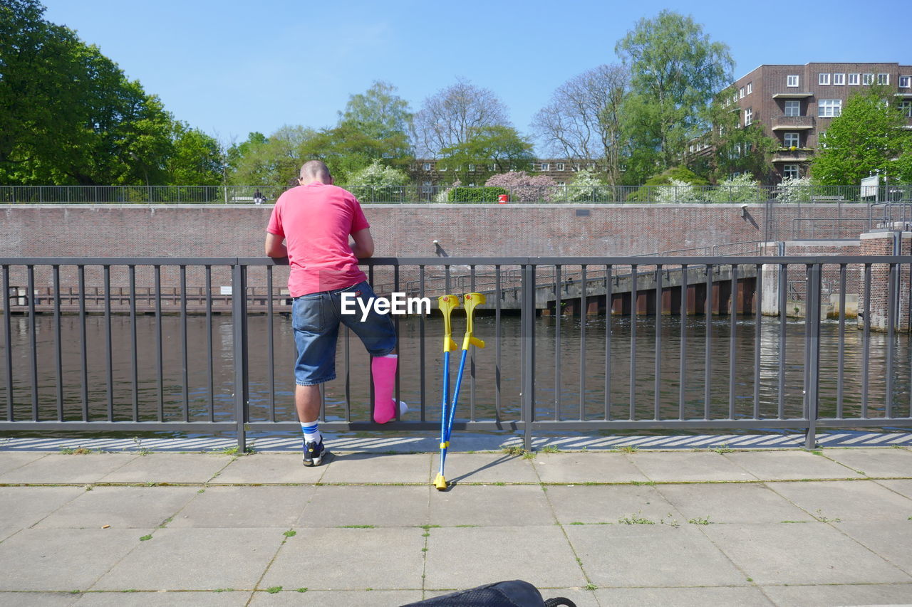 Rear view of man with broken leg standing by railing