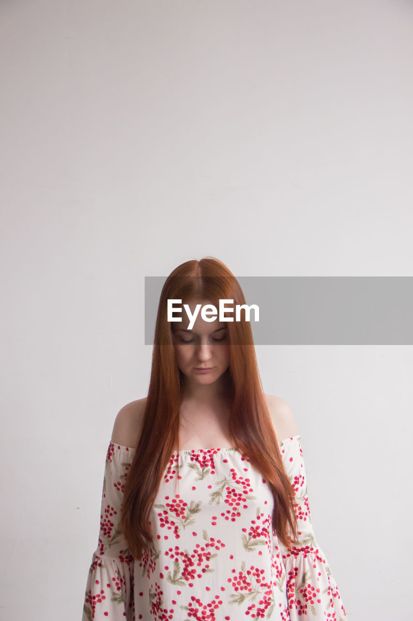 PORTRAIT OF YOUNG WOMAN AGAINST WALL