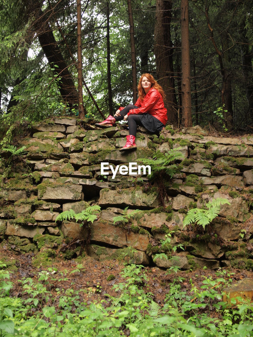 Portrait of woman sitting on stone wall in forest during monsoon