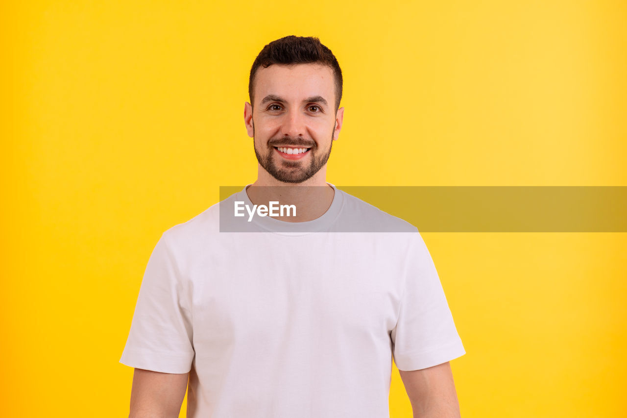 yellow, t-shirt, portrait, smiling, one person, adult, happiness, colored background, casual clothing, beard, facial hair, studio shot, looking at camera, men, yellow background, young adult, front view, waist up, emotion, indoors, standing, copy space, teeth, smile, clothing, sleeve, cheerful, person, active shirt, lifestyles, orange color, individuality, positive emotion, orange