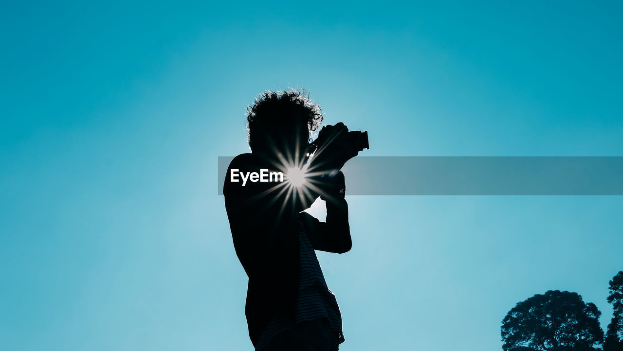 Low angle view of silhouette person against blue sky on sunny day