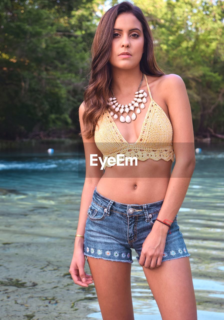 Portrait of beautiful young woman standing against lake