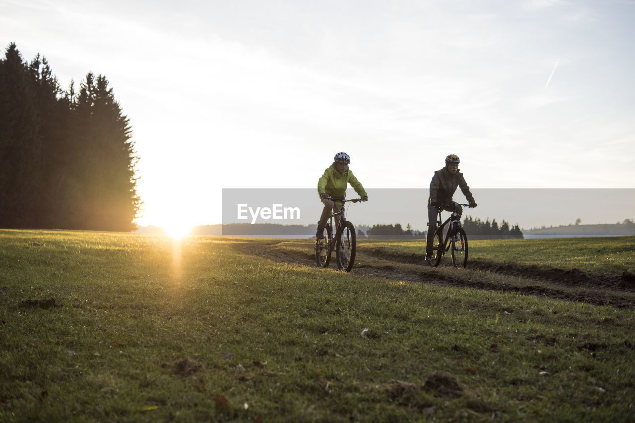 MEN RIDING BICYCLE ON GRASSLAND AGAINST SKY