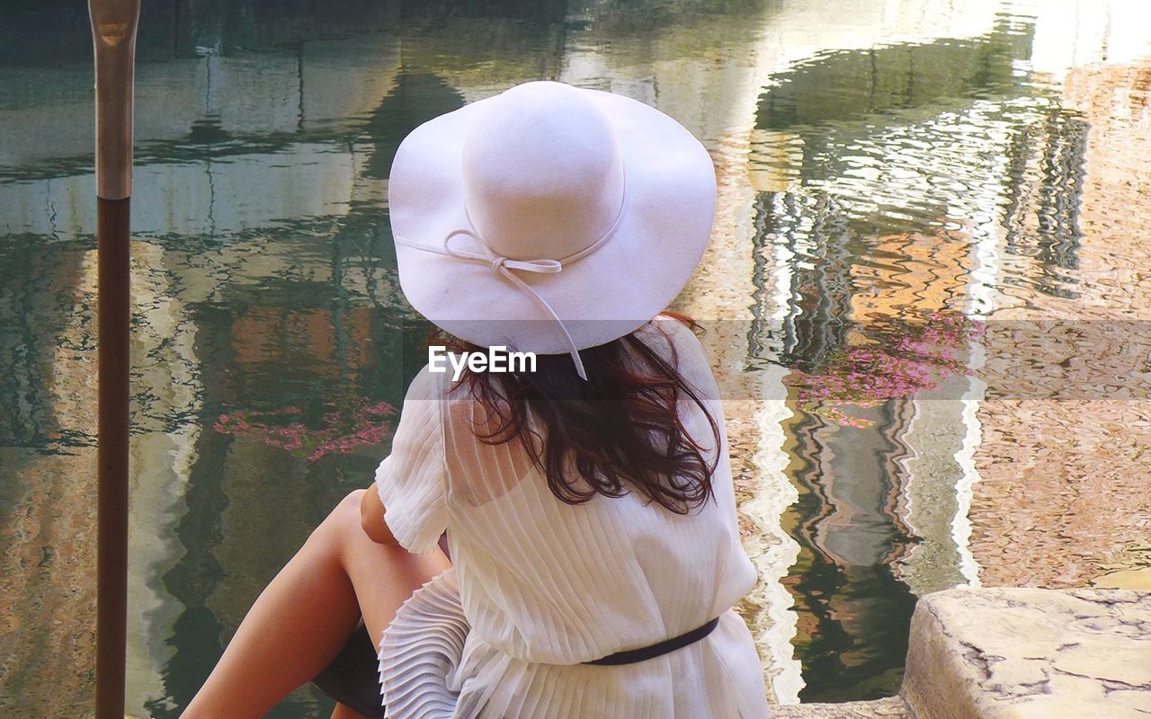 Rear view of woman wearing hat relaxing at lakeshore