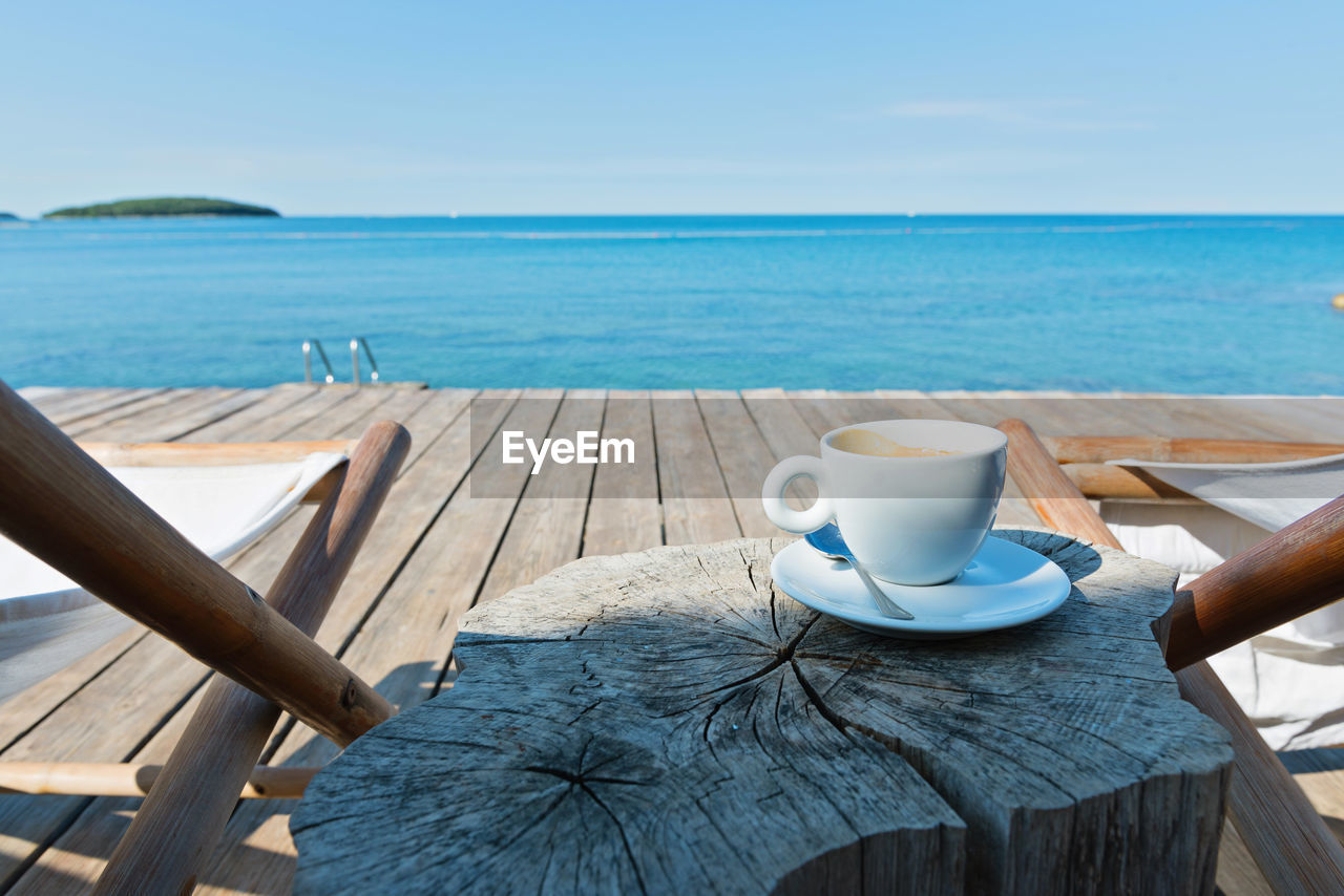 CLOSE-UP OF COFFEE ON TABLE BY SEA AGAINST SKY