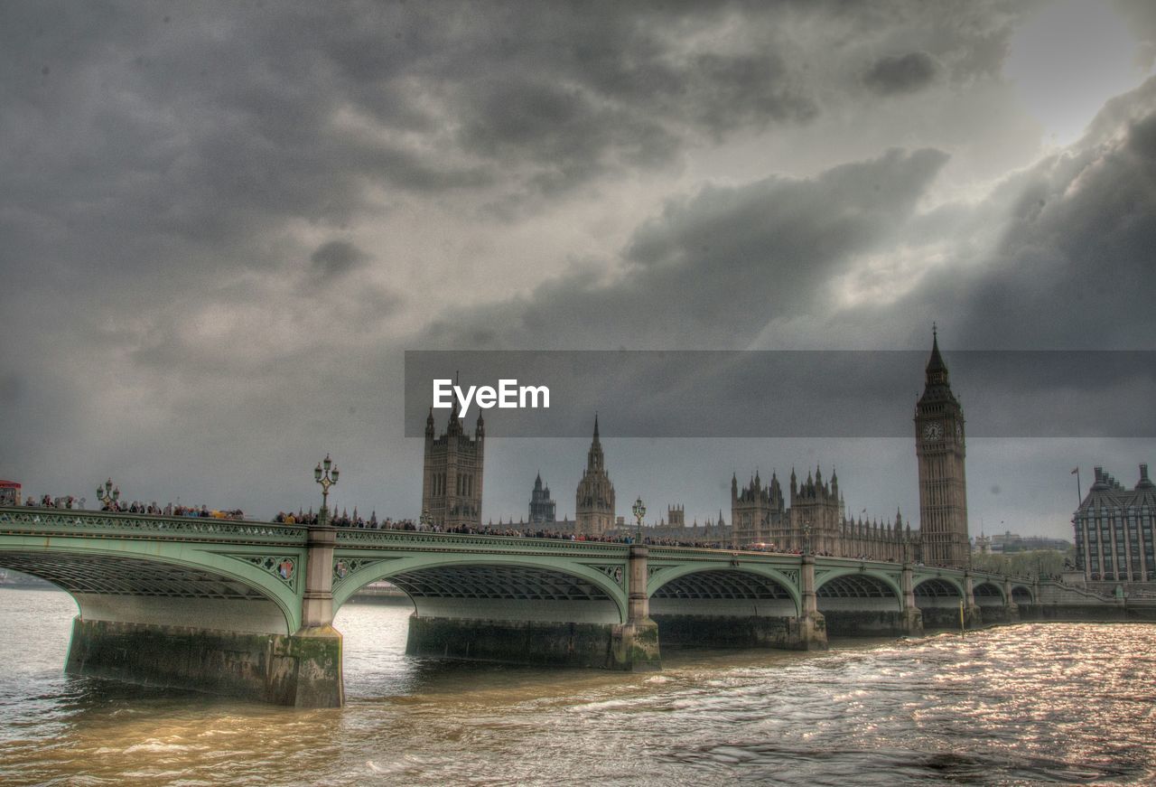 Westminster bridge over thames river against cloudy sky