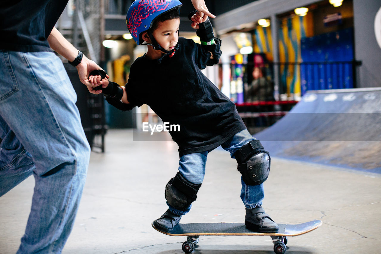 Close up of young skateboarder boy holding onto instructor's hands