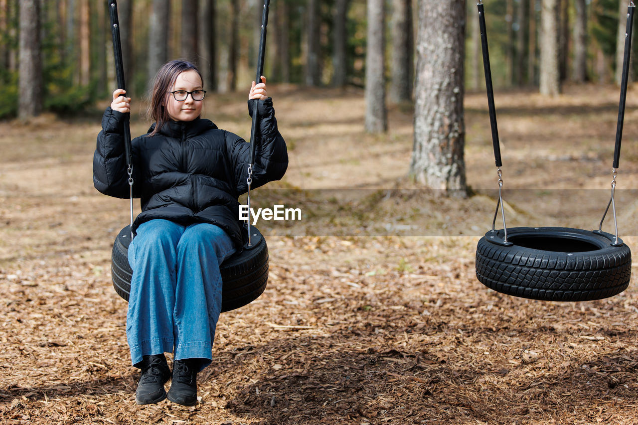 Girl outdoors on wooden ecological playground in forest park in spring, playing.