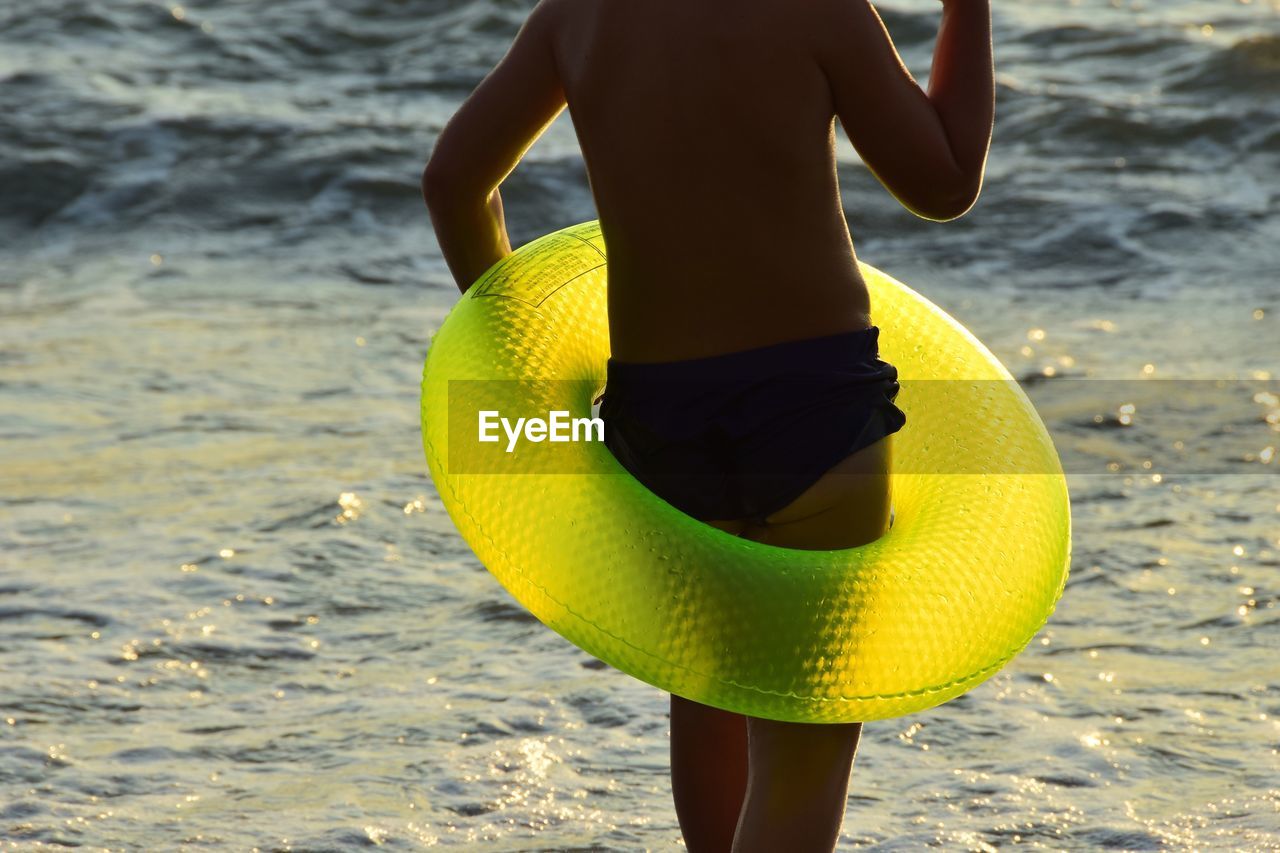 Midsection of man with inflatable ring standing at beach