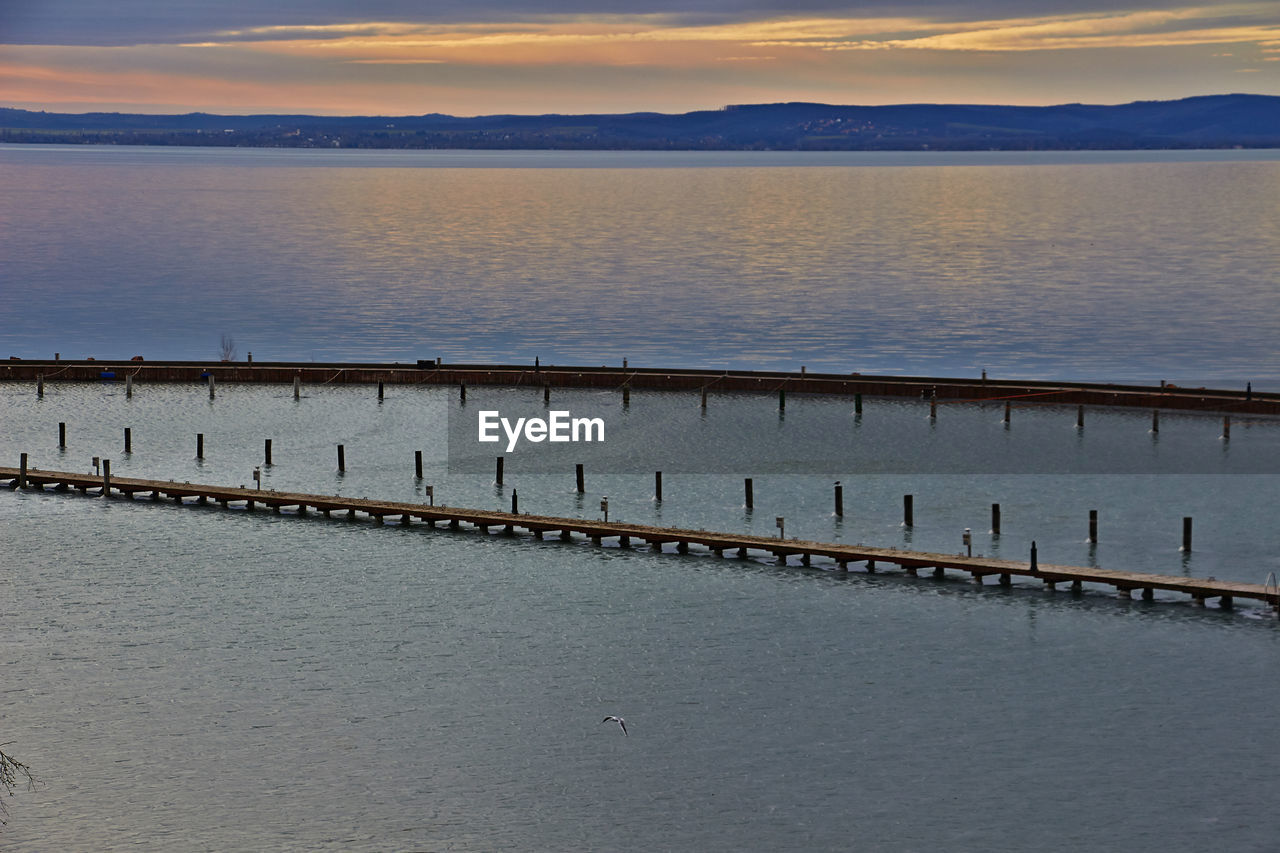 BIRDS PERCHING ON GROYNE BY SEA AGAINST SKY