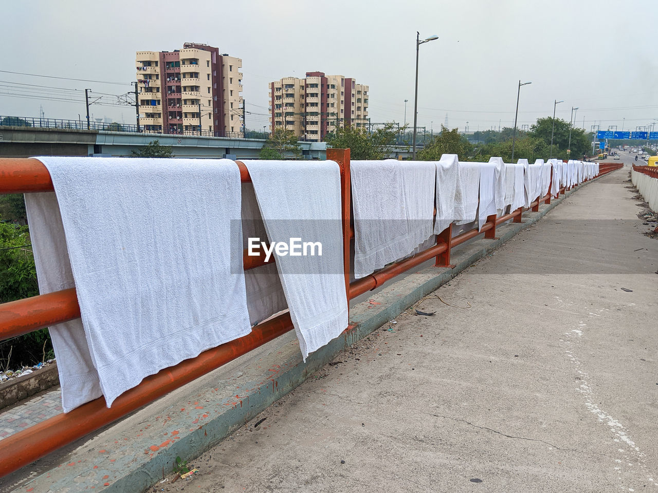 White towels drying on footpath by building next to highway against sky