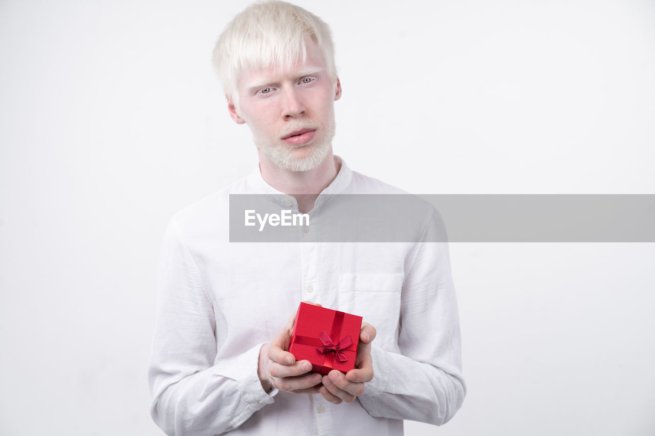 Portrait of man with albino holding christmas present against white background