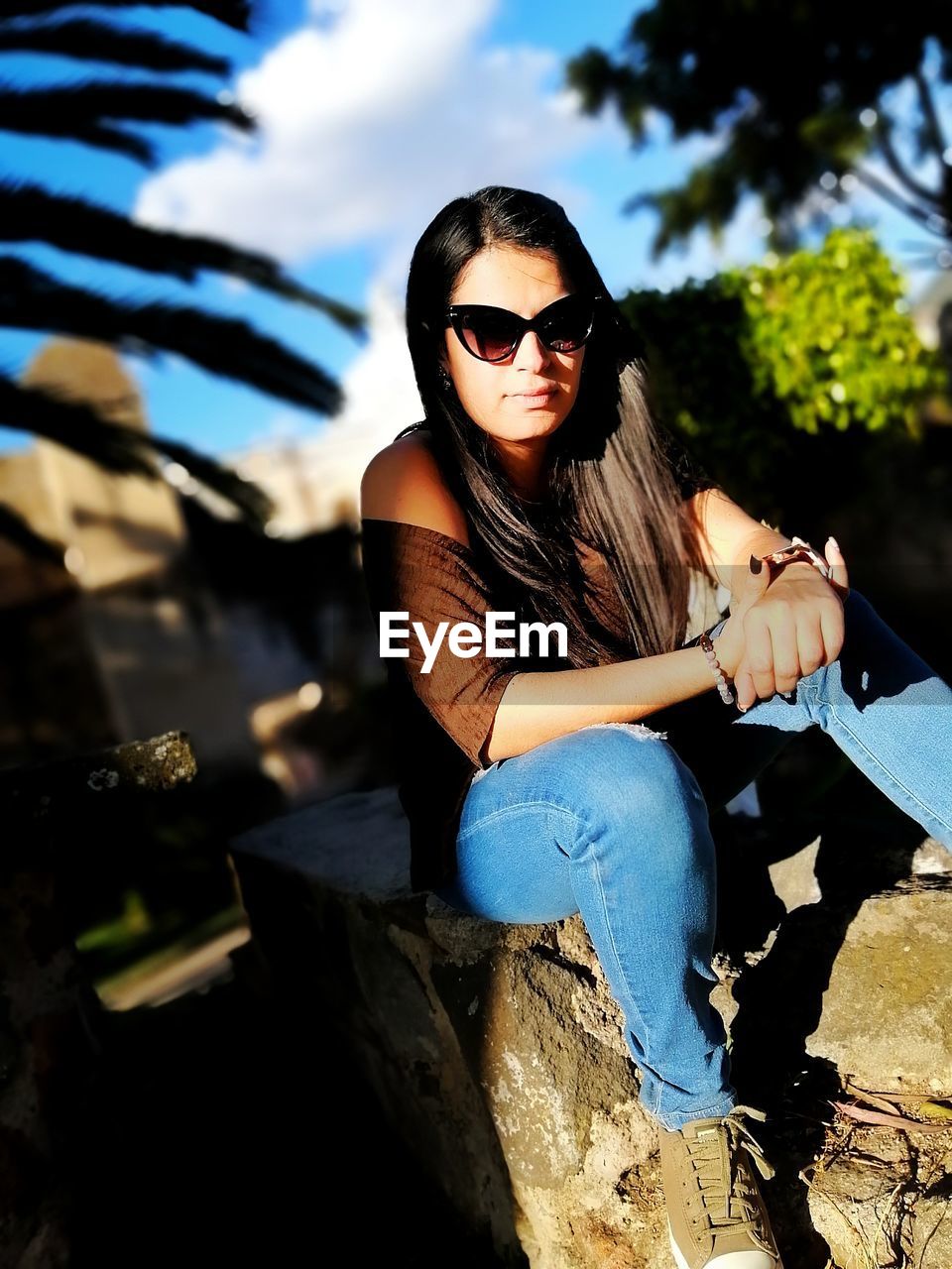 Portrait of young woman wearing sunglasses sitting while sitting outdoors