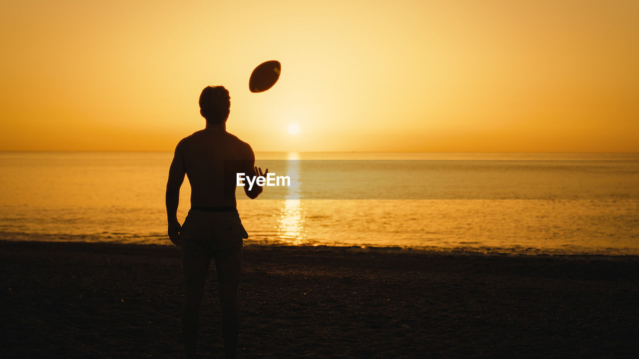 Silhouette of a man at sunset with american football ball