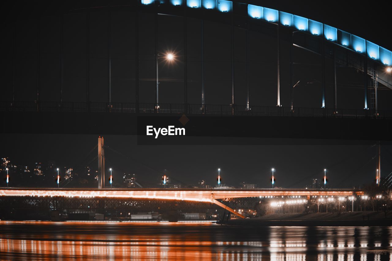 Illuminated bridge over river in city at night