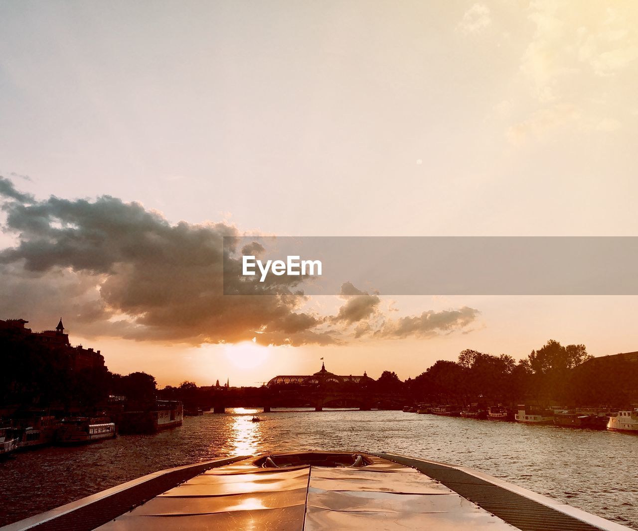 River seine in paris by silhouette trees against sky during sunset