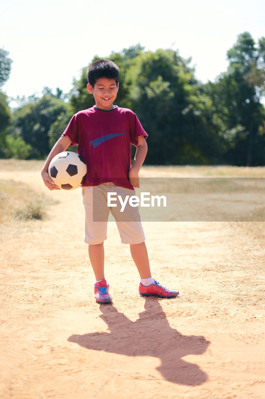 Smiling boy holding soccer ball while standing on field