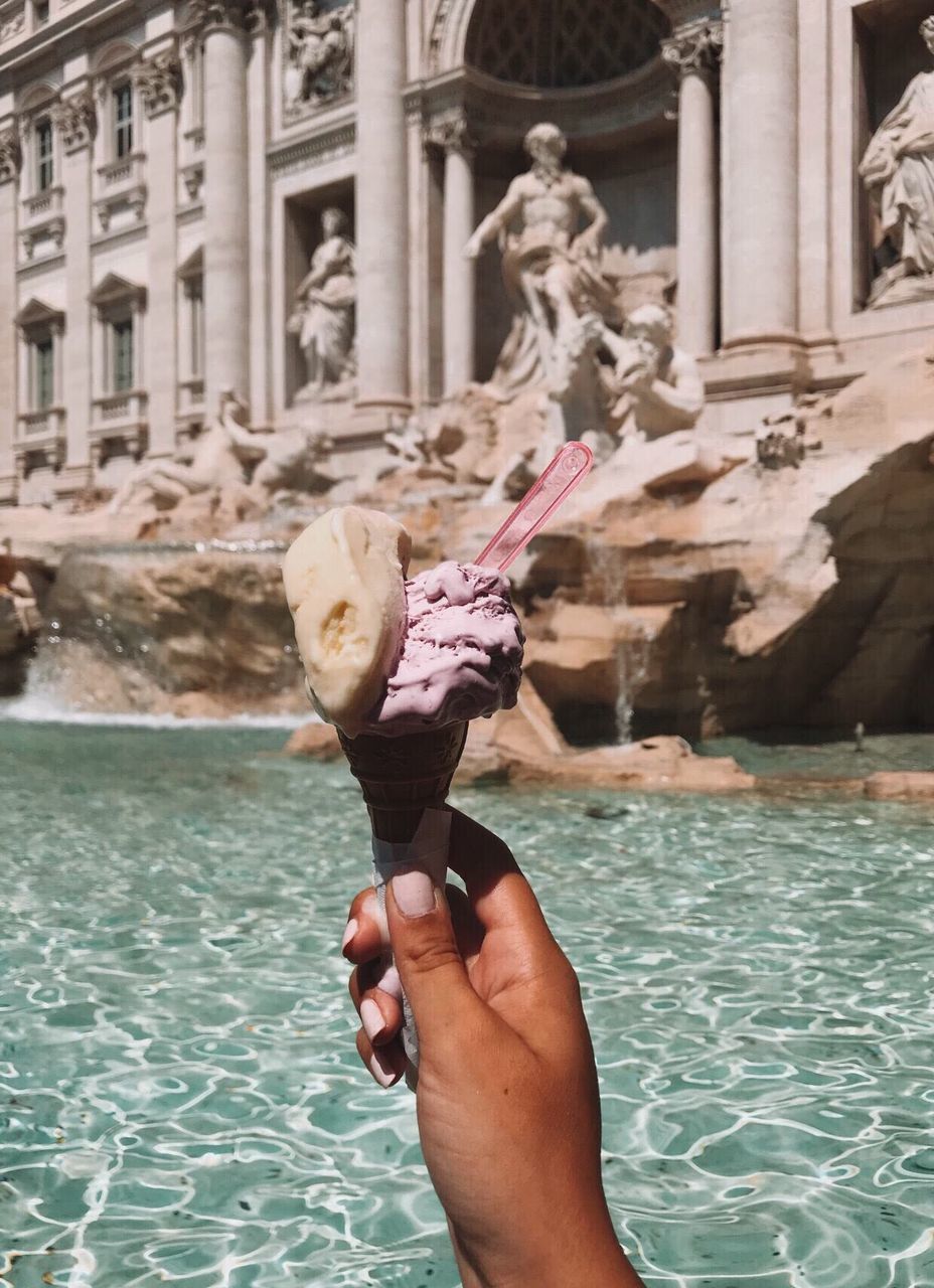 Cropped hand of woman holding ice cream against lake