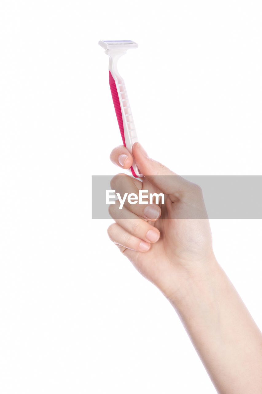 Close-up of hand holding razor against white background