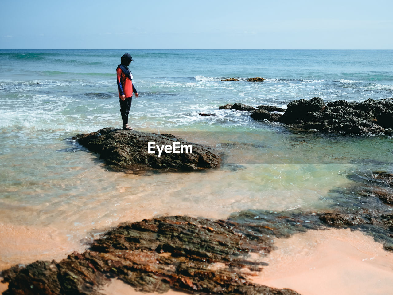 Side view of a girl standing on the rocks by the beach