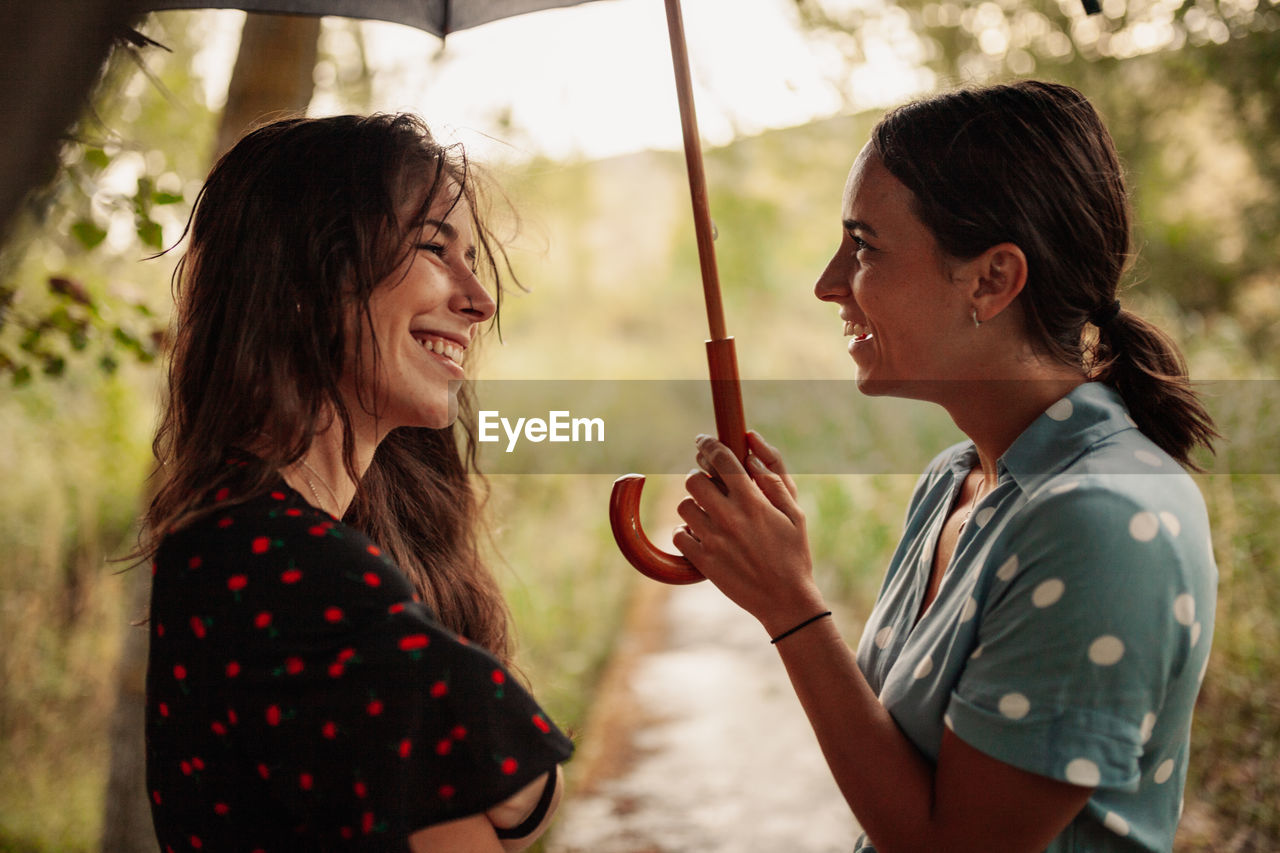 Side view of lesbian couple laughing while standing under umbrella