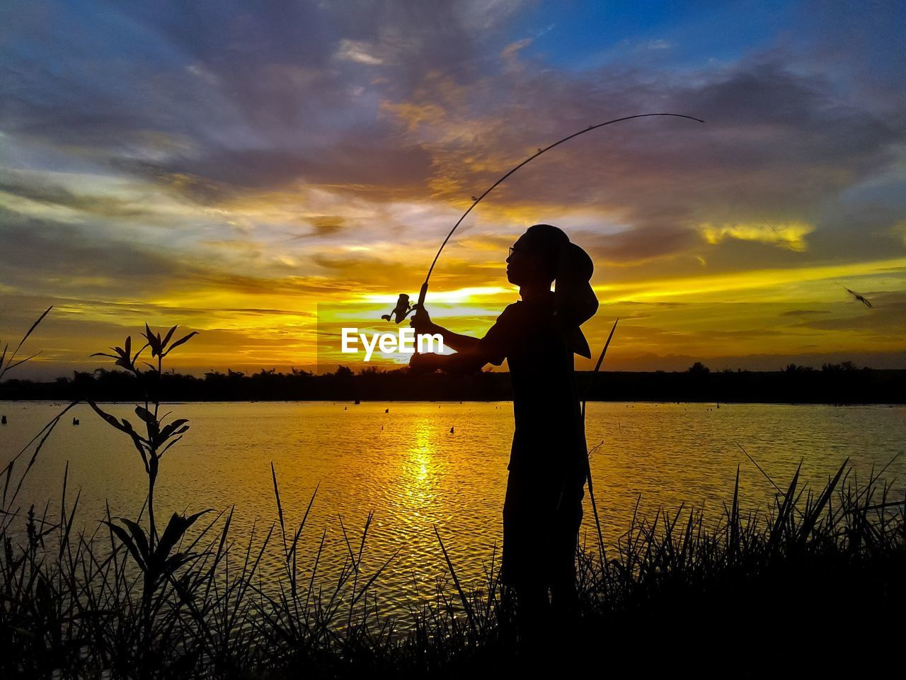 Silhouette woman fishing by lake against sky during sunset