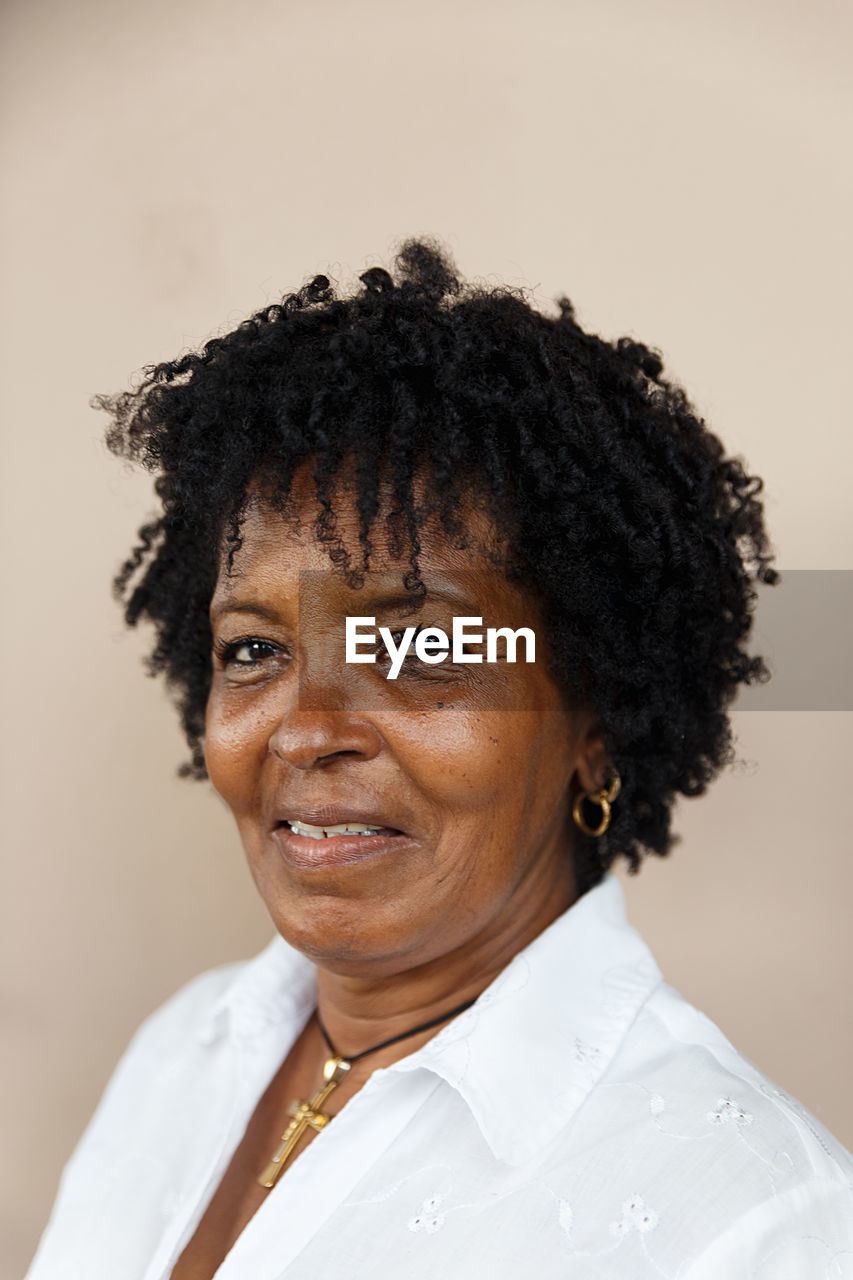 Close-up portrait of smiling mature woman against wall