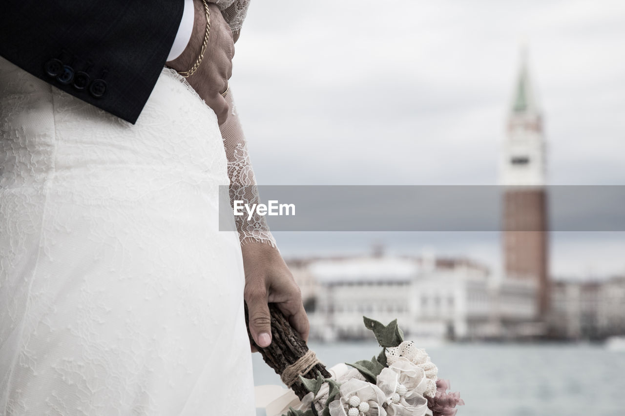 Cropped hand of bridegroom touching bride stomach against canal