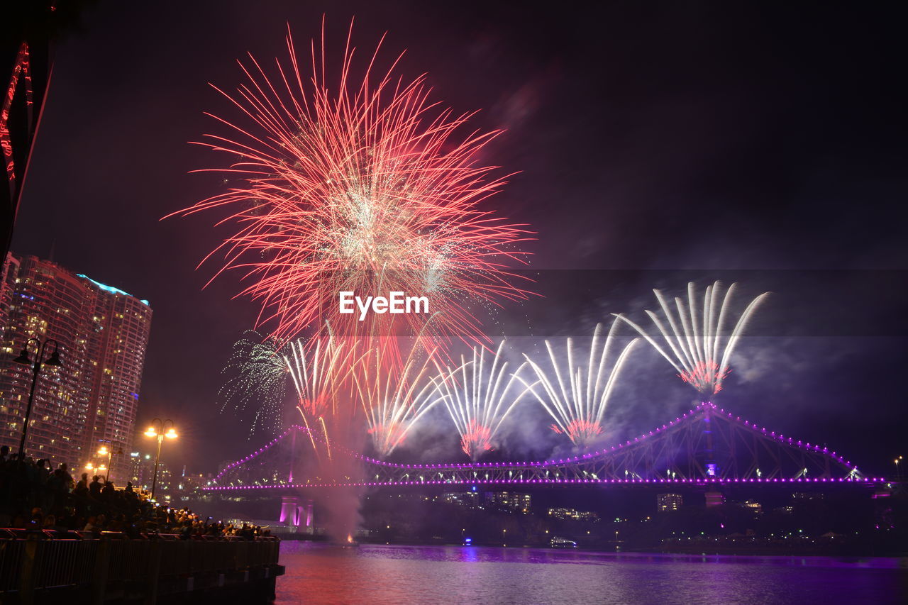 Firework display over river against sky in city at night