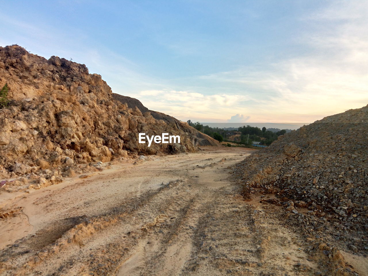 Dirt road leading towards mountains against sky