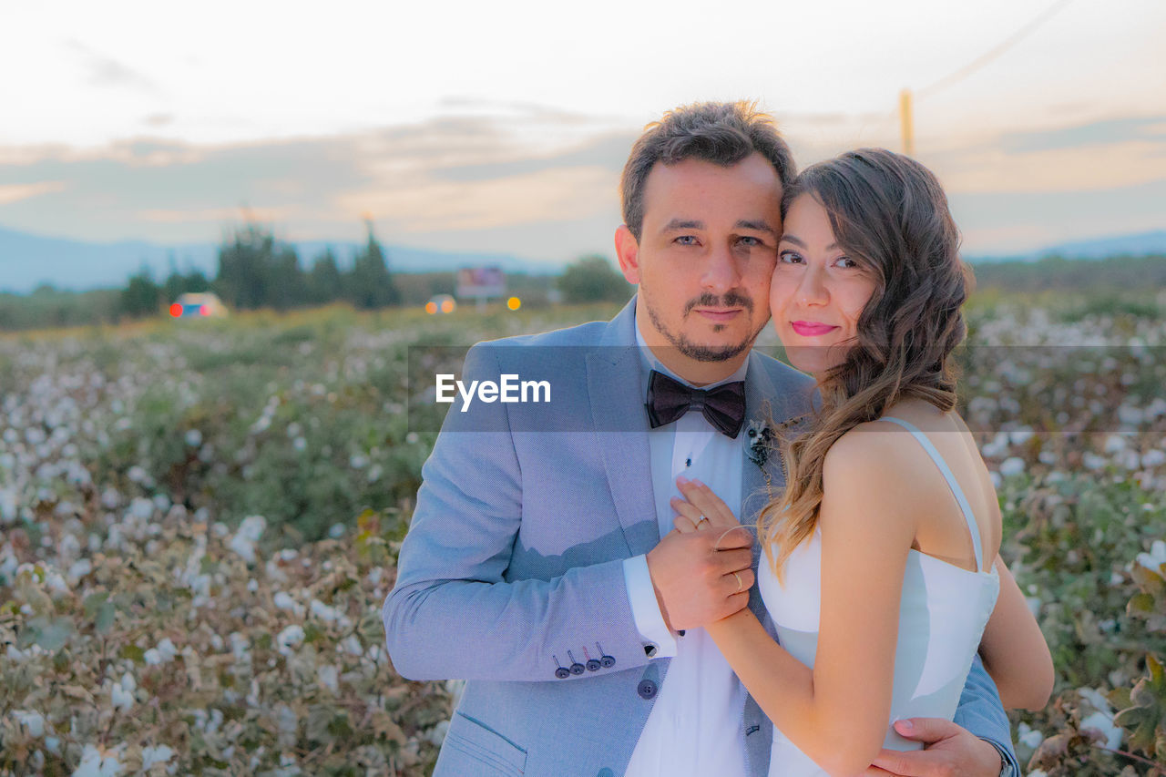 Portrait of smiling bride and groom standing on field