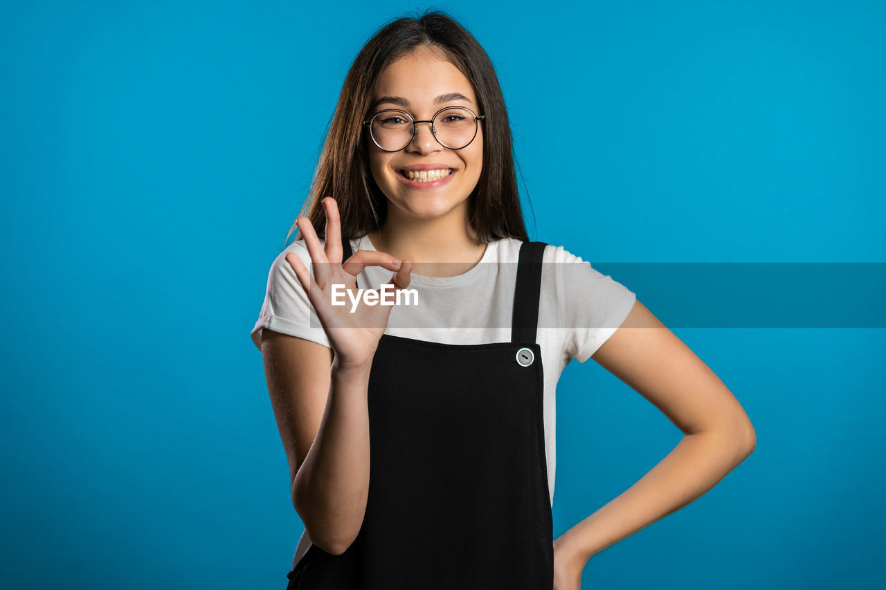 PORTRAIT OF A SMILING YOUNG WOMAN AGAINST BLUE BACKGROUND