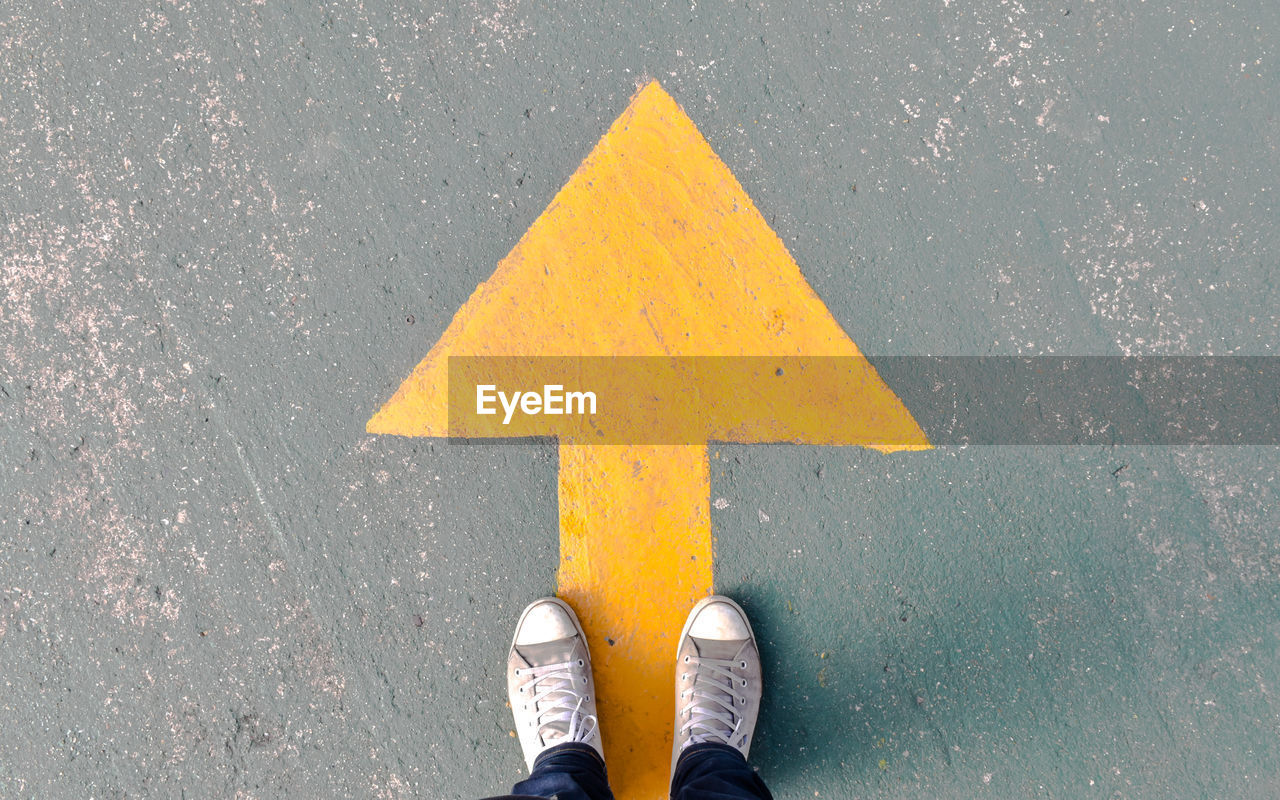 Low section of man standing on street by arrow symbol