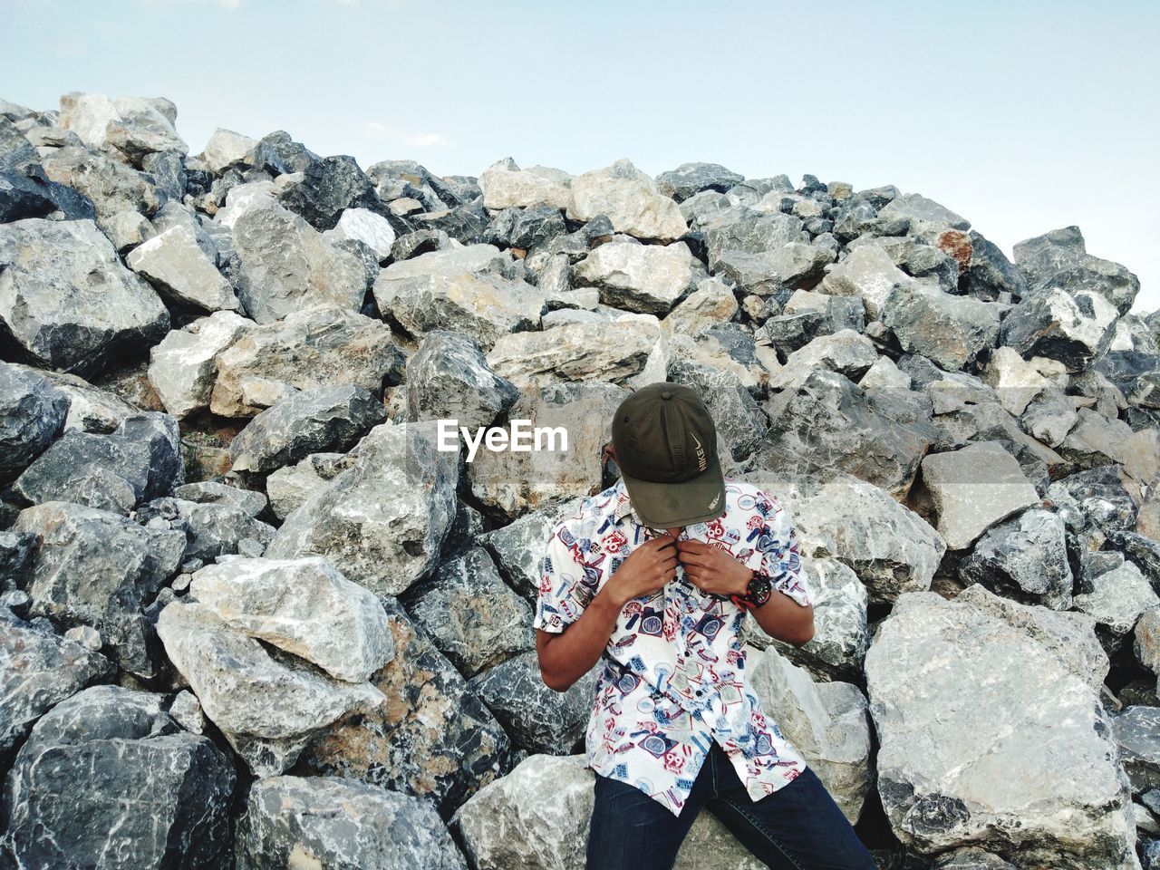 REAR VIEW OF WOMAN STANDING ON ROCK AGAINST SKY