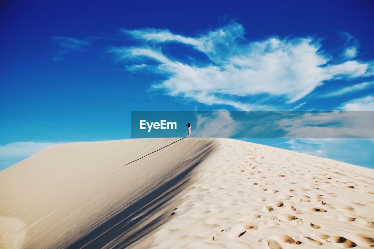 Woman standing in desert against blue sky