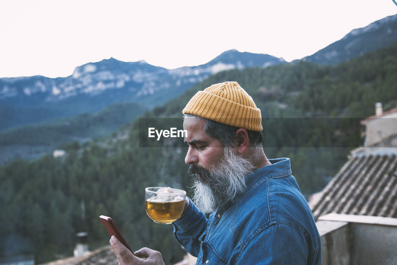 Man on his smartphone with a cup of coffee in the mountains. independent man. remote work