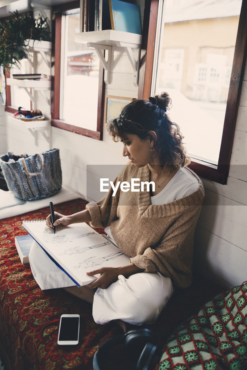 Mid adult woman drawing sketch in book at houseboat
