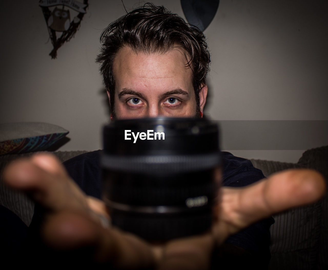 Portrait of man showing lens while sitting on sofa at home