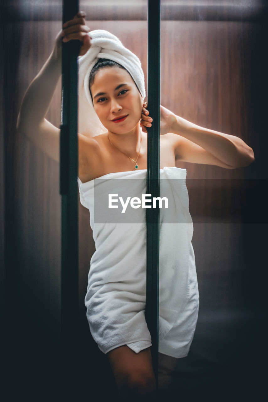 Portrait of woman wrapped in towel while standing at home