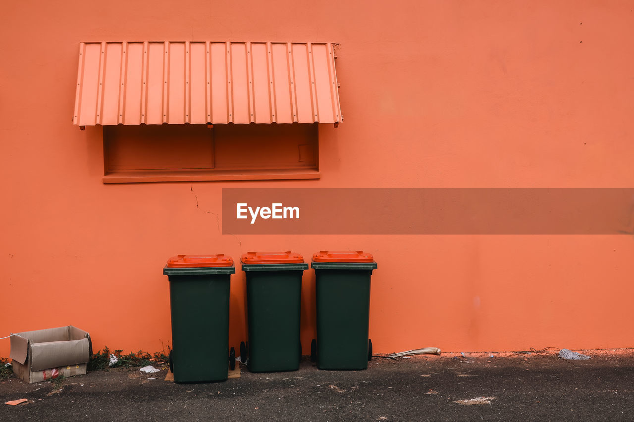 Three garbage bins in front of orange colored building