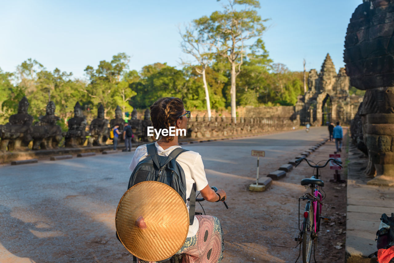 Rear view of woman riding bicycle on road against sky