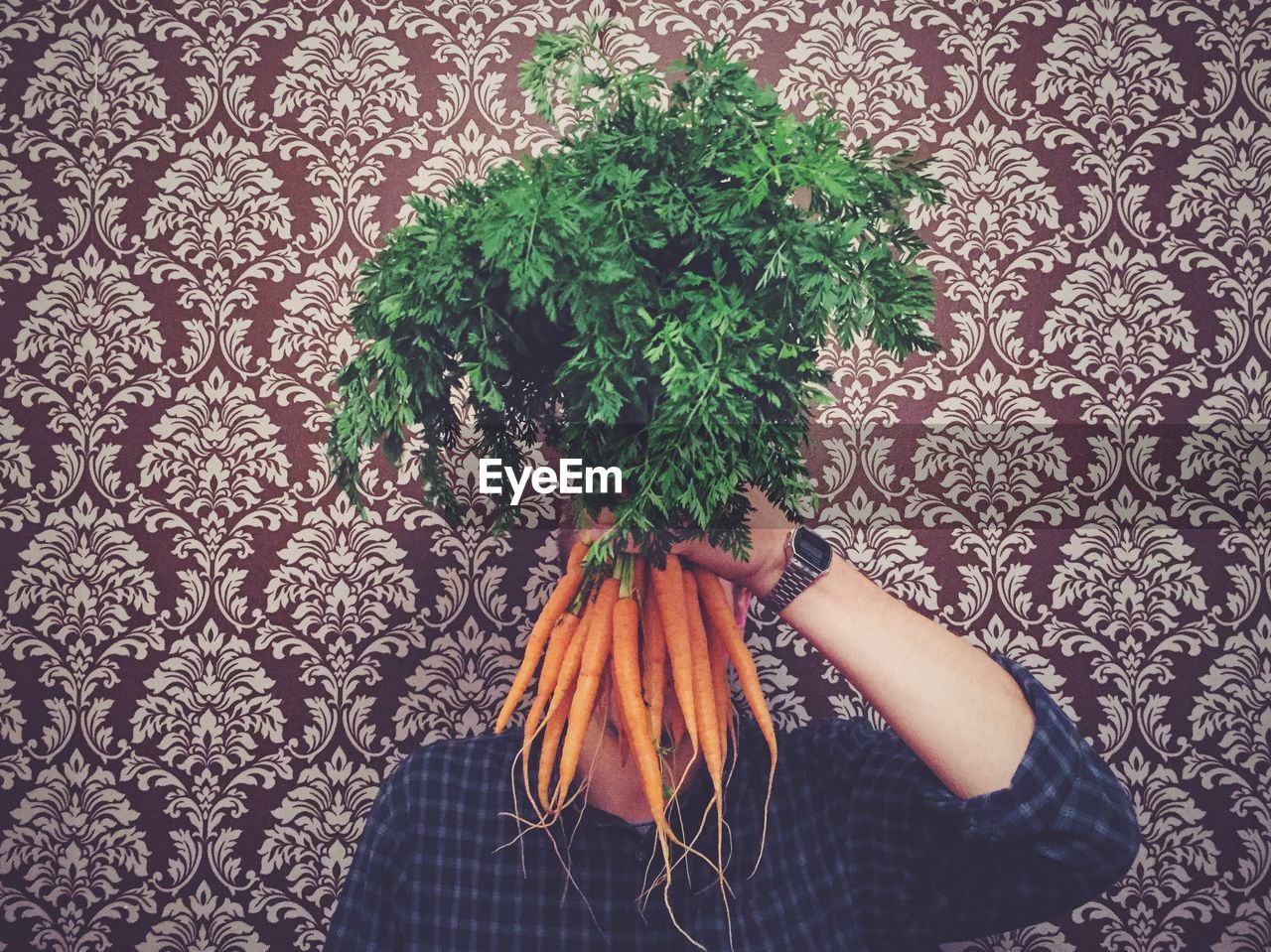 Person holding carrots against patterned wall