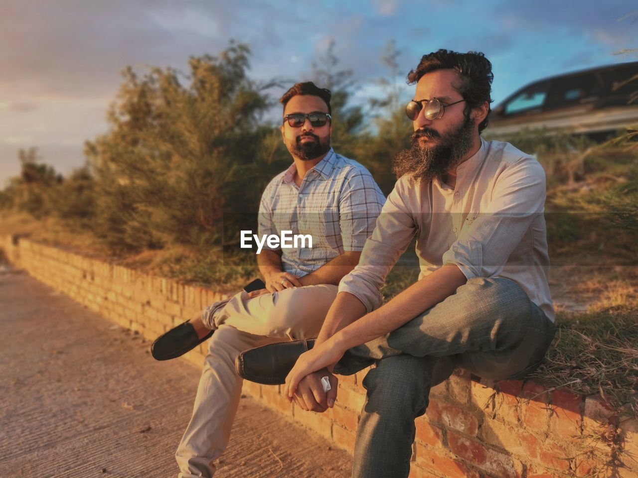 Portrait of two mid adult men sitting and hanging out together on a small wall during sunset